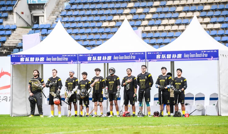 Malaysian lacrosse lining up at sidelines to sing national anthem before face-off.